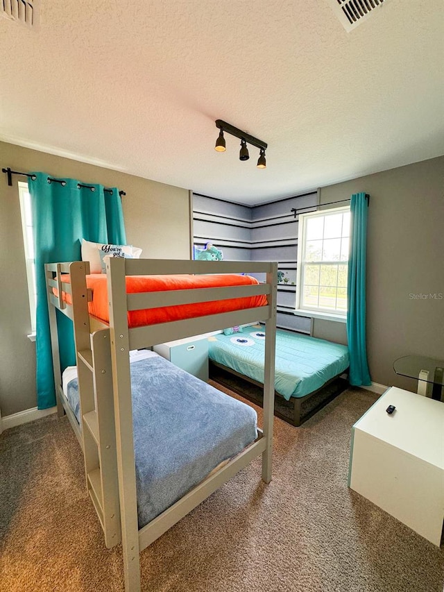 bedroom with track lighting, a textured ceiling, and carpet flooring