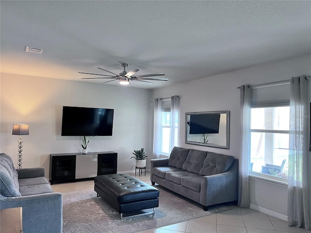 living room with a ceiling fan, a wealth of natural light, visible vents, and light tile patterned flooring