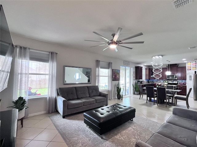 living area featuring light tile patterned floors, baseboards, visible vents, and ceiling fan with notable chandelier