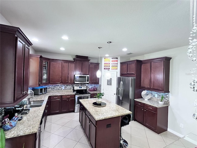 kitchen with light tile patterned flooring, stainless steel appliances, a kitchen island, a sink, and backsplash