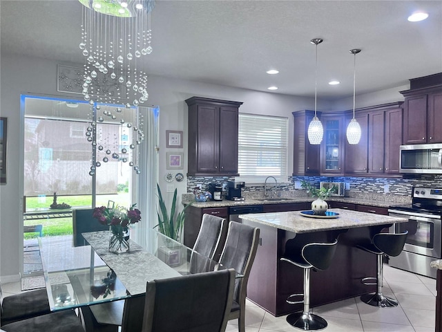 kitchen with light tile patterned floors, light stone counters, appliances with stainless steel finishes, a sink, and backsplash