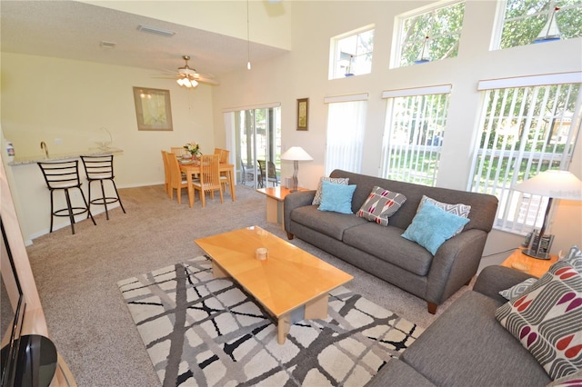 carpeted living room with a wealth of natural light, a towering ceiling, and ceiling fan