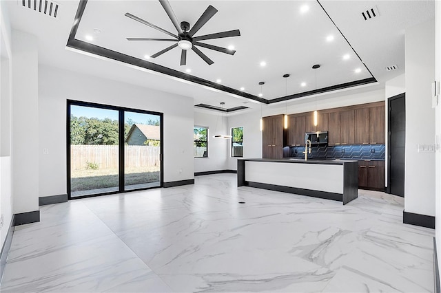 kitchen featuring sink, decorative light fixtures, a center island with sink, a raised ceiling, and decorative backsplash