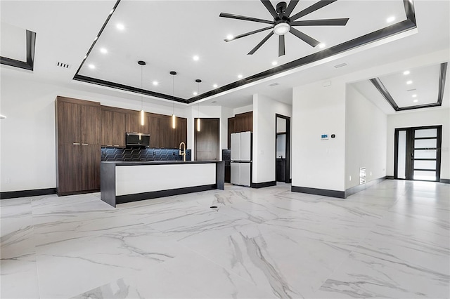 kitchen with hanging light fixtures, white refrigerator, tasteful backsplash, a tray ceiling, and a center island with sink