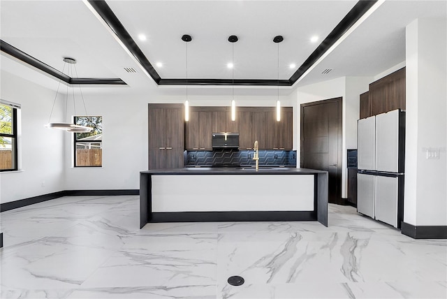 kitchen featuring dark brown cabinets, fridge, a tray ceiling, pendant lighting, and backsplash