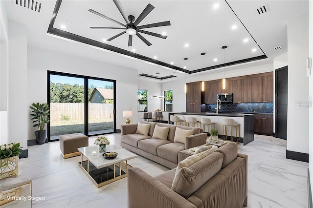 living room with sink, ceiling fan, and a tray ceiling