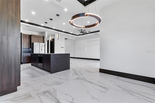 kitchen with white refrigerator, an island with sink, a tray ceiling, and decorative light fixtures