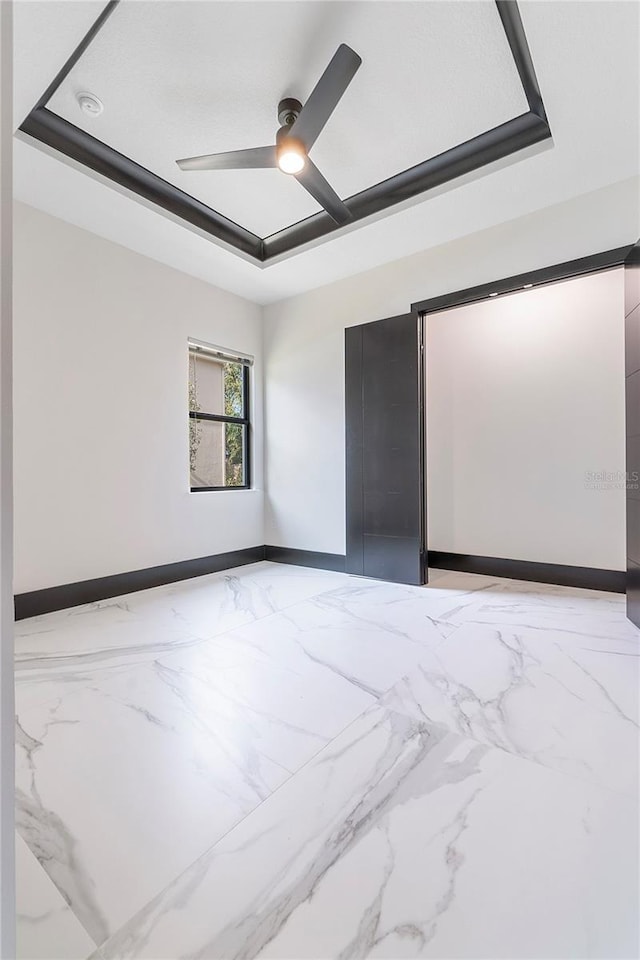 empty room with ceiling fan and a tray ceiling