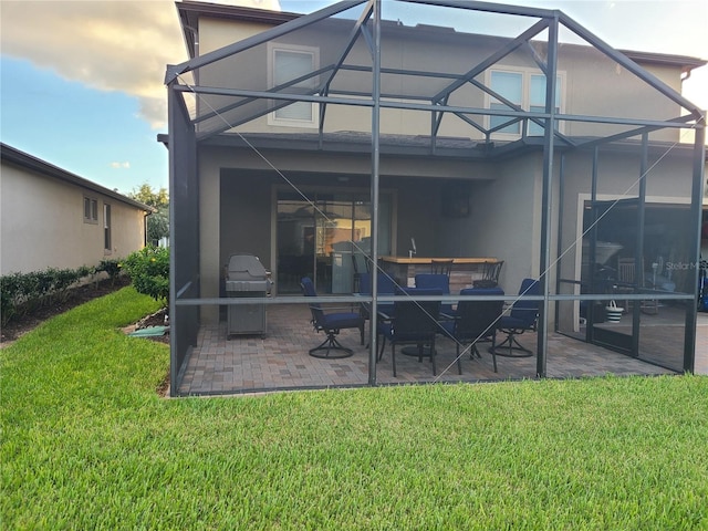 back of property with a yard, a patio area, and glass enclosure