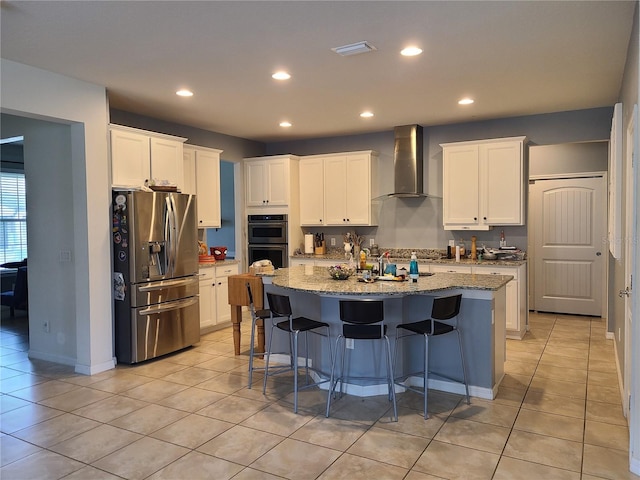 kitchen with a kitchen island with sink, stainless steel refrigerator with ice dispenser, light stone countertops, white cabinets, and wall chimney exhaust hood