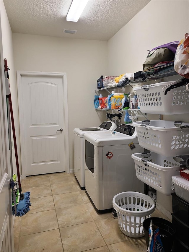 clothes washing area with light tile patterned floors, washing machine and clothes dryer, and a textured ceiling