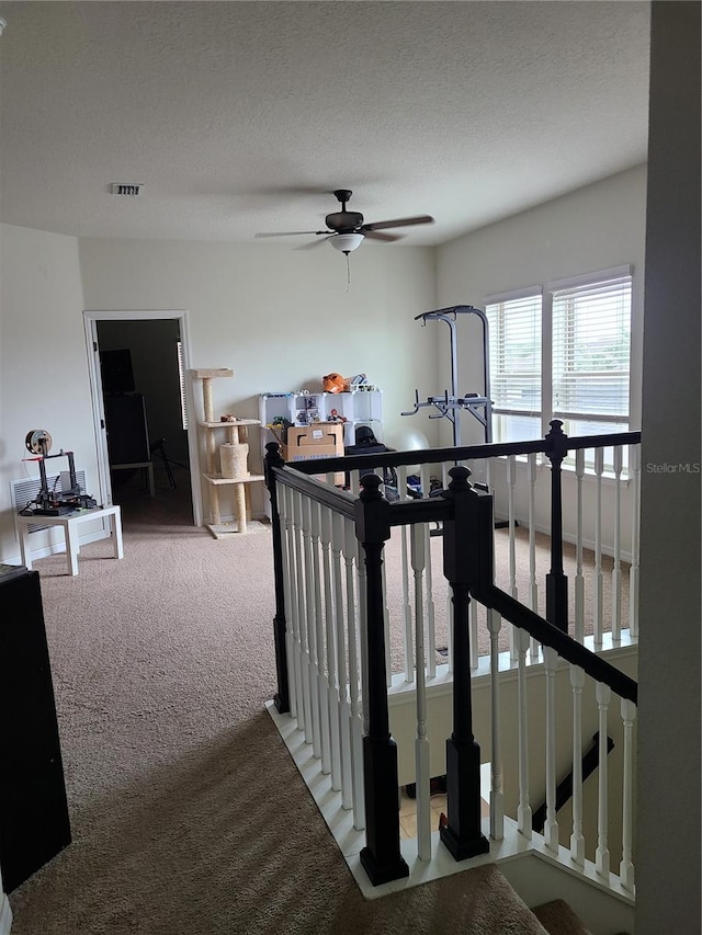 stairs with ceiling fan, carpet flooring, and a textured ceiling