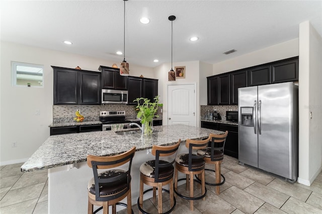 kitchen with decorative light fixtures, stainless steel appliances, light stone countertops, a breakfast bar, and a center island with sink