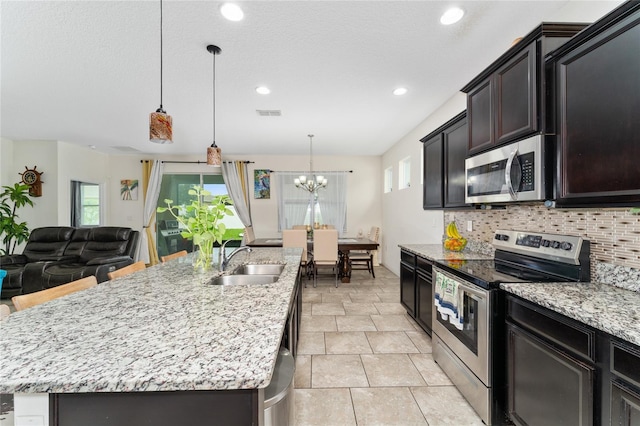 kitchen with decorative light fixtures, stainless steel appliances, an island with sink, and sink