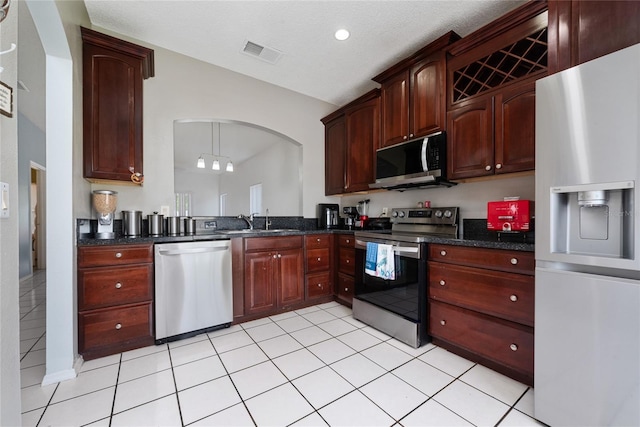 kitchen featuring light tile patterned flooring, appliances with stainless steel finishes, sink, dark stone countertops, and hanging light fixtures