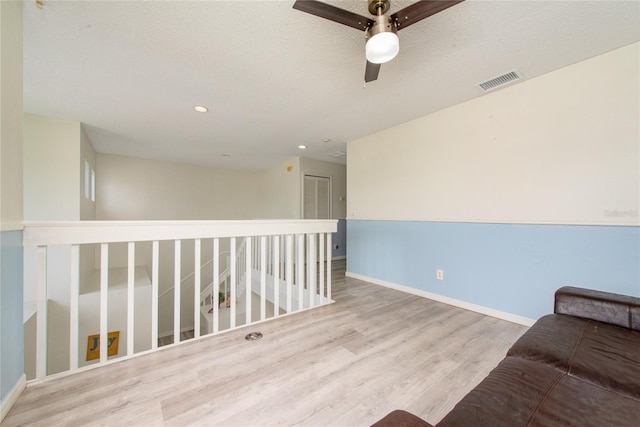 living area with a textured ceiling, ceiling fan, and light hardwood / wood-style flooring