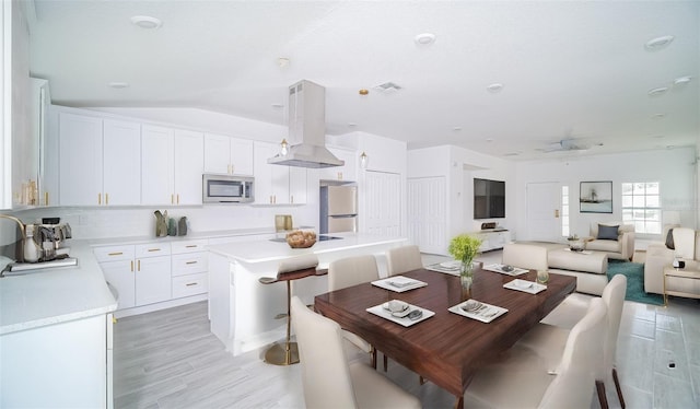 kitchen with appliances with stainless steel finishes, white cabinetry, island exhaust hood, and a center island