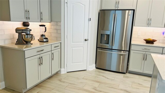 kitchen featuring light stone countertops, stainless steel refrigerator with ice dispenser, light wood-type flooring, and tasteful backsplash