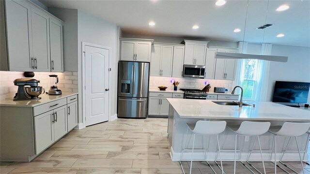 kitchen featuring an island with sink, backsplash, appliances with stainless steel finishes, and sink