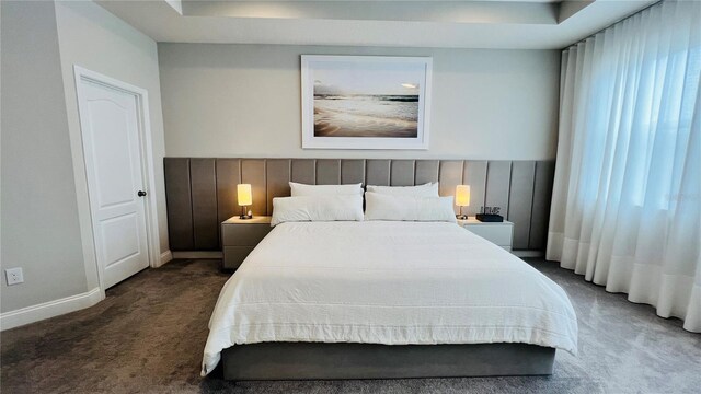 bedroom with dark colored carpet and a tray ceiling