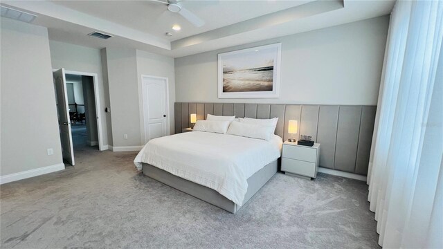 bedroom featuring a raised ceiling, ceiling fan, and light colored carpet