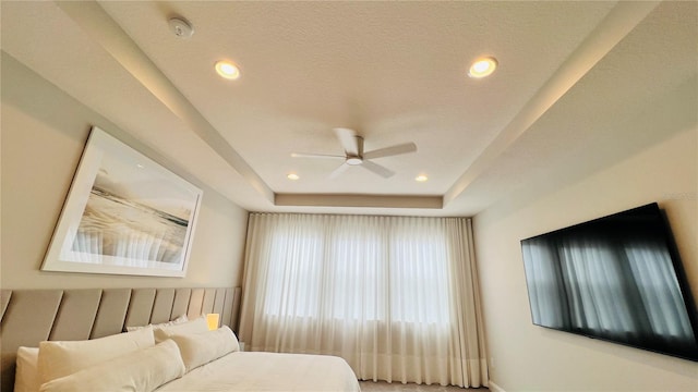 bedroom with a textured ceiling, a tray ceiling, and ceiling fan