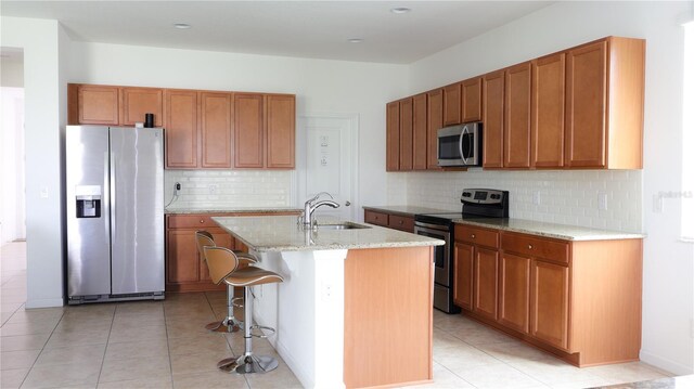 kitchen with a breakfast bar, light stone counters, sink, stainless steel appliances, and a center island with sink