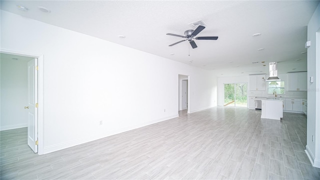 unfurnished living room with light wood-type flooring, visible vents, ceiling fan, and a sink