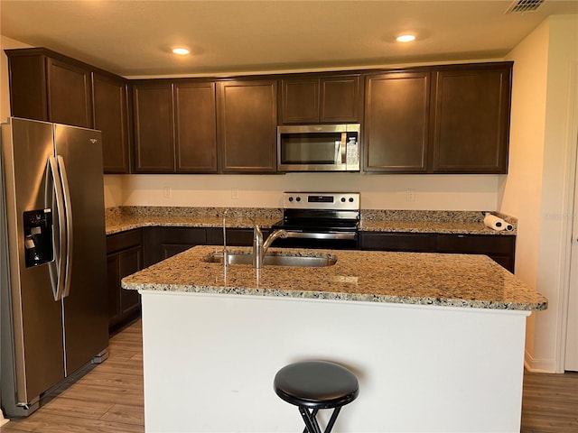 kitchen featuring appliances with stainless steel finishes, light stone counters, light hardwood / wood-style floors, sink, and an island with sink