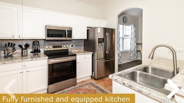kitchen with a sink, arched walkways, stainless steel appliances, white cabinetry, and tasteful backsplash