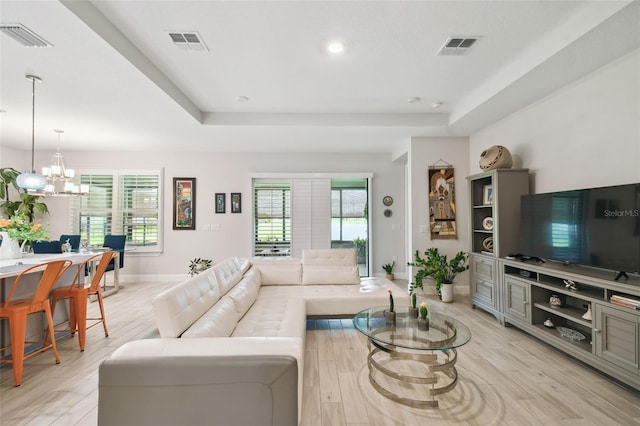 living room featuring plenty of natural light, a raised ceiling, light wood-type flooring, and a chandelier