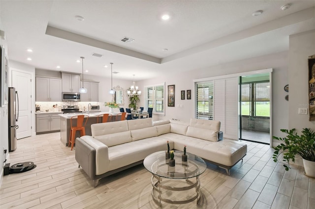 living room with a tray ceiling, light hardwood / wood-style flooring, sink, and a notable chandelier