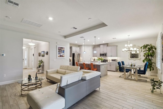 living room with light wood-type flooring, a raised ceiling, an inviting chandelier, and sink