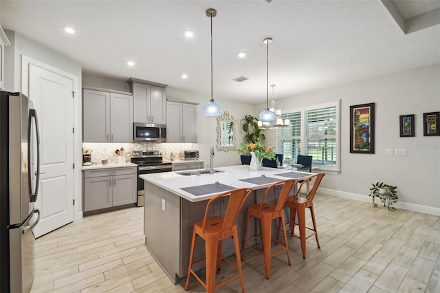 kitchen featuring gray cabinetry, stainless steel appliances, sink, an island with sink, and pendant lighting