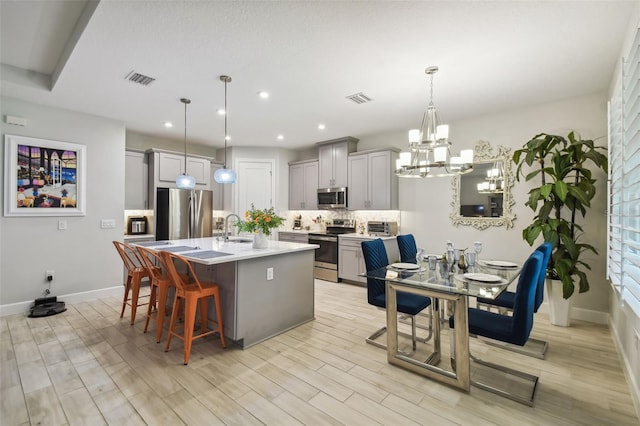 kitchen with a kitchen island with sink, light hardwood / wood-style flooring, decorative light fixtures, stainless steel appliances, and a breakfast bar area