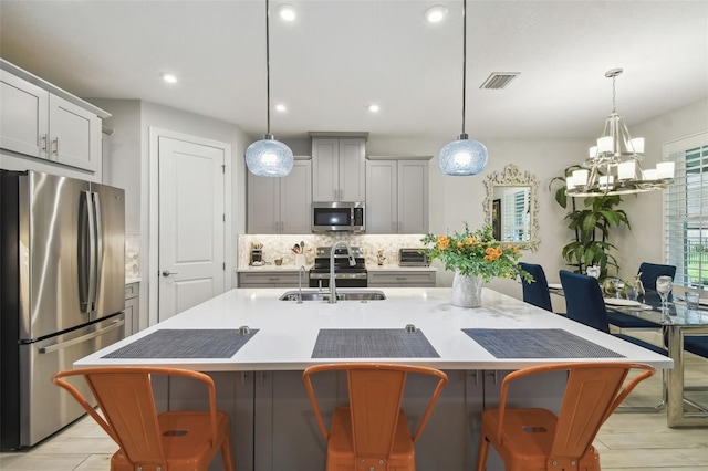 kitchen featuring a breakfast bar area, a center island with sink, a notable chandelier, appliances with stainless steel finishes, and light wood-type flooring