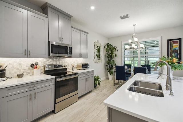 kitchen featuring gray cabinetry, a notable chandelier, light hardwood / wood-style floors, stainless steel appliances, and sink