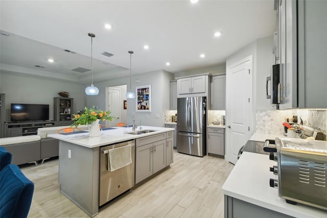 kitchen with gray cabinets, appliances with stainless steel finishes, and an island with sink