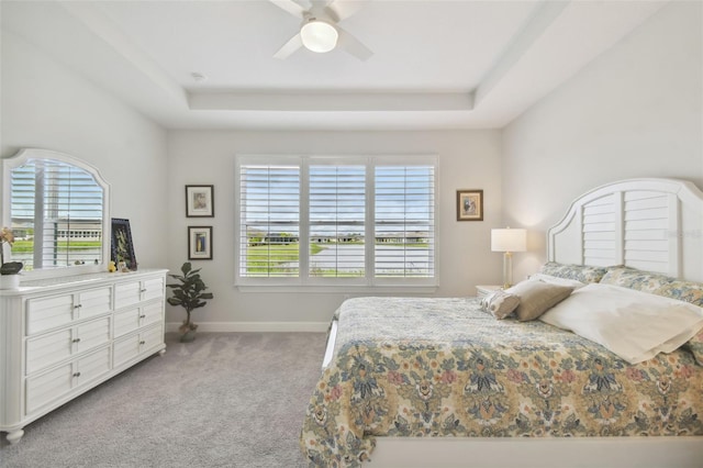 bedroom with light colored carpet, ceiling fan, a tray ceiling, and multiple windows