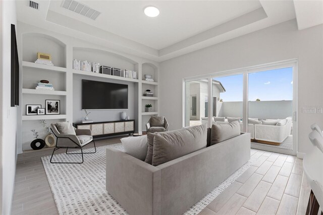 living room with built in shelves and a raised ceiling