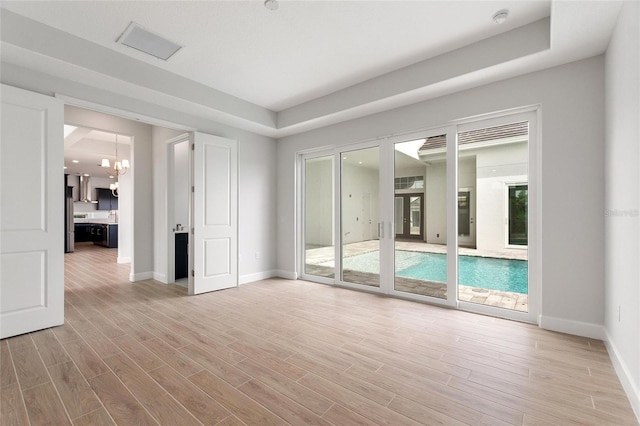 unfurnished room featuring an inviting chandelier and light wood-type flooring