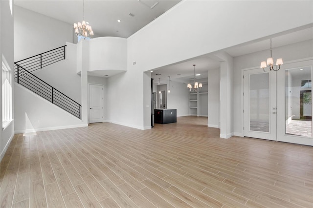 unfurnished living room with an inviting chandelier, a towering ceiling, french doors, and light wood-type flooring