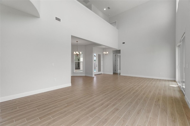 unfurnished living room featuring light wood-type flooring, a high ceiling, and a notable chandelier