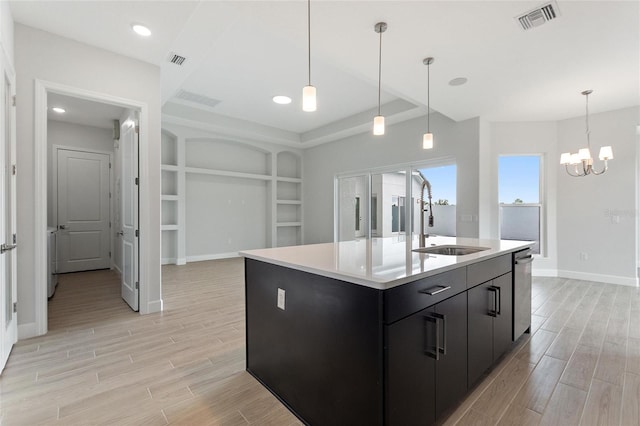 kitchen with built in shelves, a kitchen island with sink, sink, and hanging light fixtures