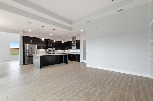 kitchen featuring pendant lighting, wall chimney range hood, stainless steel fridge, light hardwood / wood-style floors, and an island with sink