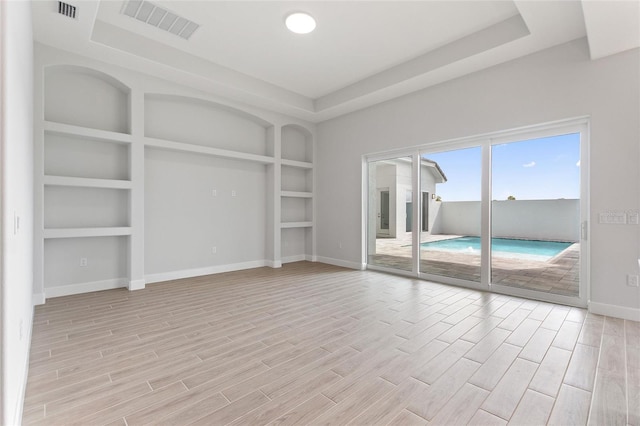 unfurnished living room featuring a tray ceiling, light wood-type flooring, and built in shelves