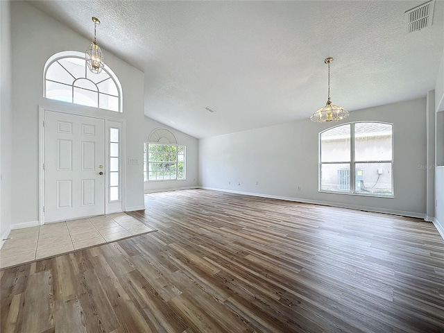 entryway with wood finished floors, baseboards, visible vents, a textured ceiling, and a notable chandelier