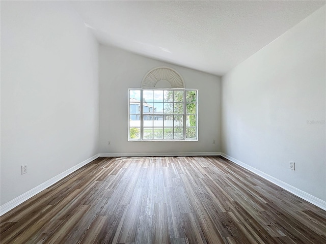 spare room featuring dark wood-style floors, a textured ceiling, baseboards, and vaulted ceiling