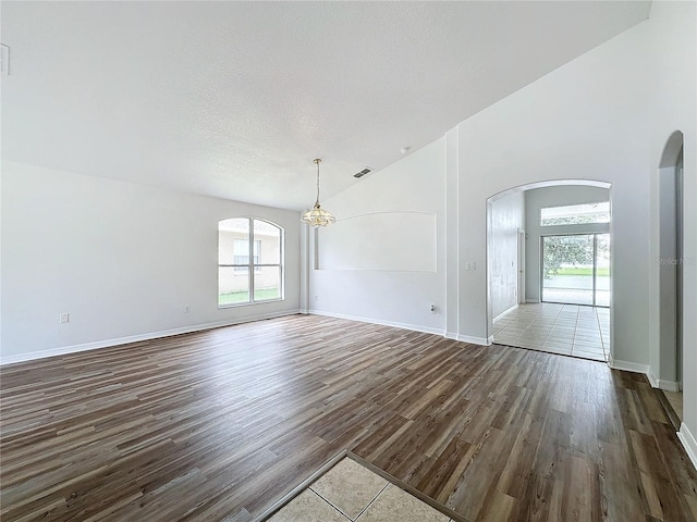 interior space featuring arched walkways, plenty of natural light, vaulted ceiling, and dark wood-type flooring