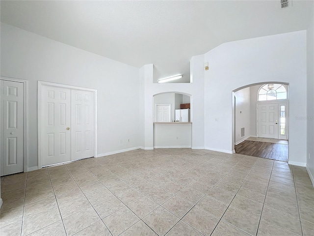 unfurnished living room featuring visible vents, baseboards, light tile patterned flooring, arched walkways, and high vaulted ceiling